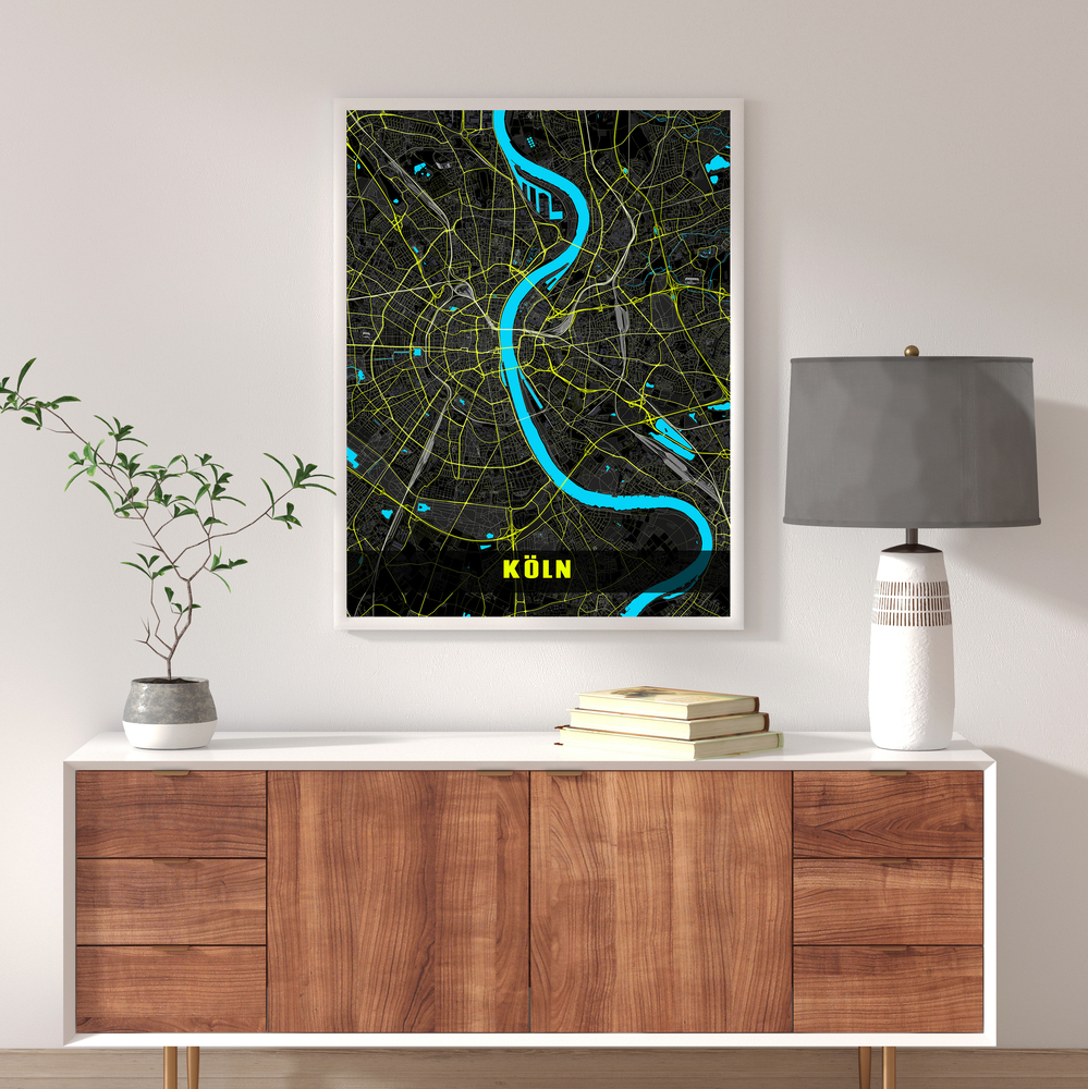 Poster con mappa di Colonia in colori neon, in cornice bianca sopra una credenza di legno accanto a una lampada