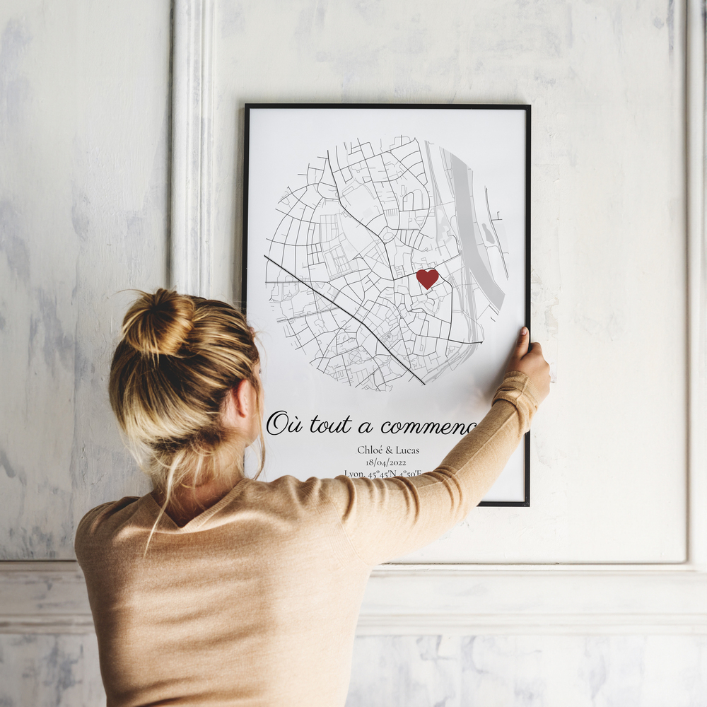 Plan de ville en cercle avec cœur rouge et prénoms personnalisés, dans un cadre noir sur un mur à moulures