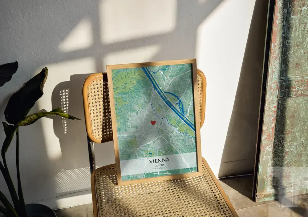 Poster con mappa urbana verde e blu e coordinate, in cornice di legno naturale su una sedia in paglia al sole