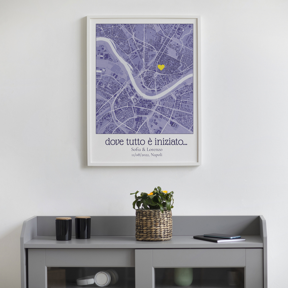 Mappa della città sui toni del lilla con cuore giallo e nomi, in cornice bianca sopra una credenza grigia